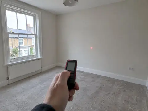 Laser distance measurer being used to measure an empty bedroom